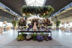 Stunning indoor wedding venue with floral arrangements and a multi-tiered cake on a decorated table. — How to Get a Vintage V