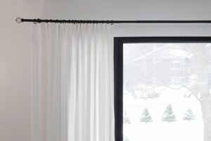 Close-up of white curtains hanging from a black curtain rod near a window, creating a modern look
