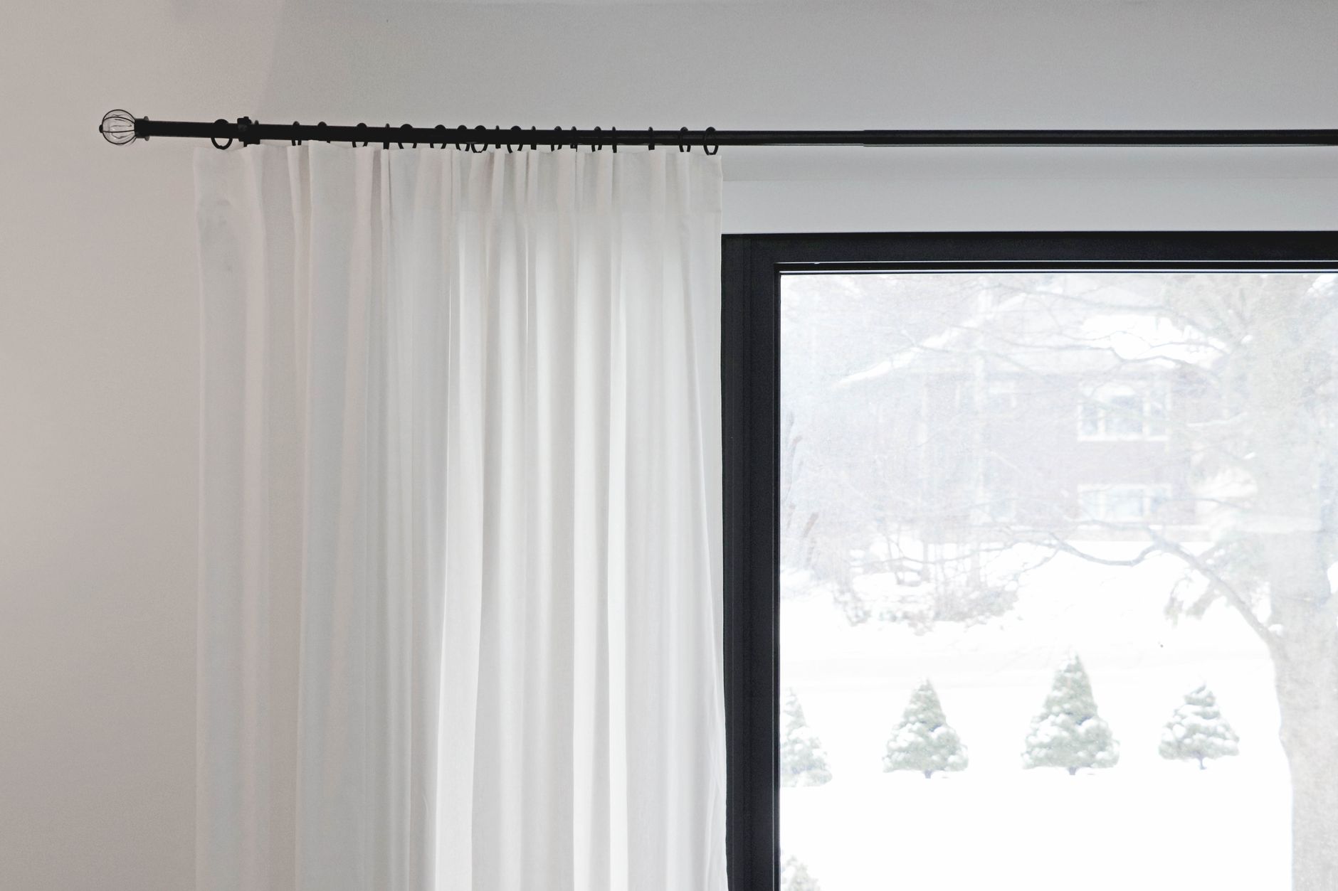 Close-up of white curtains hanging from a black curtain rod near a window, creating a modern look