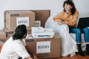 Young couple planning a home relocation with packed boxes labeled for organization and a laptop for coordination. — Ways to g